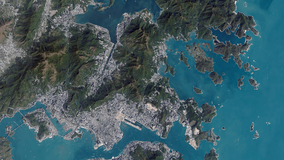 Vista de satélite de Hong Kong y el mar adyacente. La ciudad se asienta principalmente en en los valles de la zona y cercana a las costas, mientras que las montañas presentan pocas manchas urbanas.